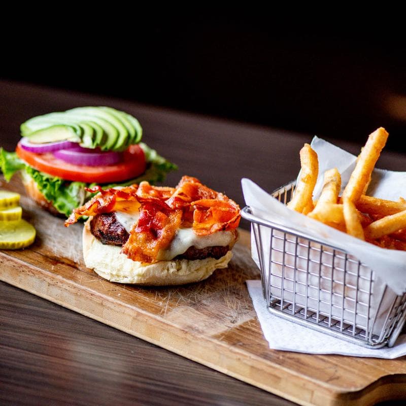 Avocado bacon burger with fries on a board